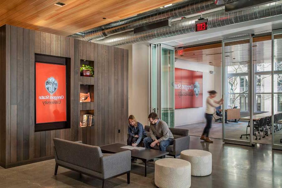people sitting in a lobby with a large screen with the Oregon State University logo