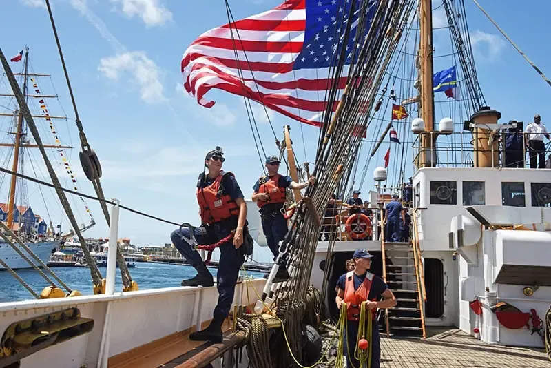 Steenson standing on the edge of a large ship with an American flag waving above her with two crewmates standing next to her
